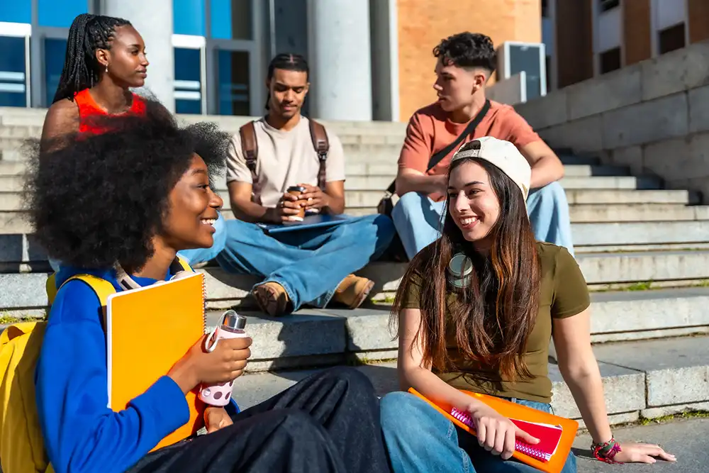 A group outside their school building chatting together on a sunny day.