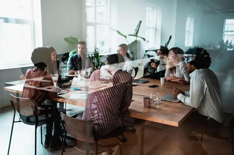 A group of business professionals meeting and seated around a wooden conference table.