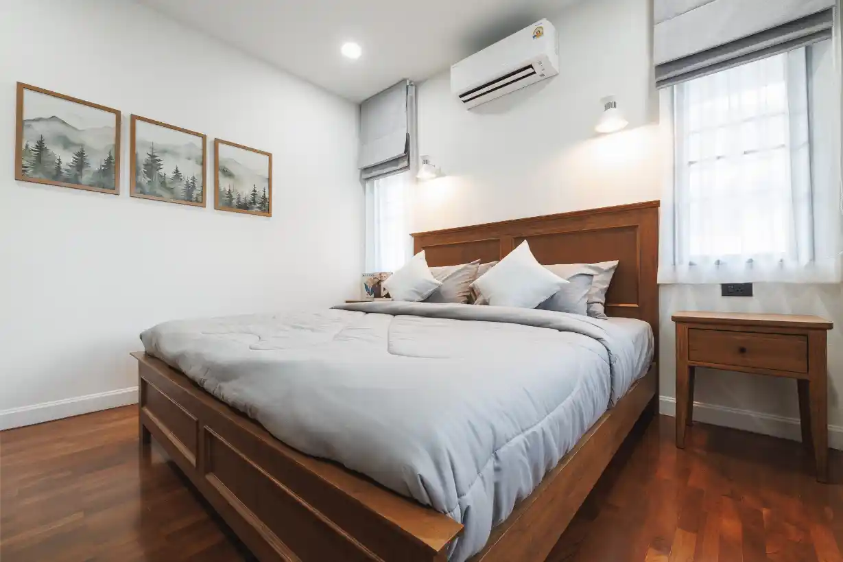A bright guest bedroom featuring a teak bed and nightstand on polished hardwood floors.