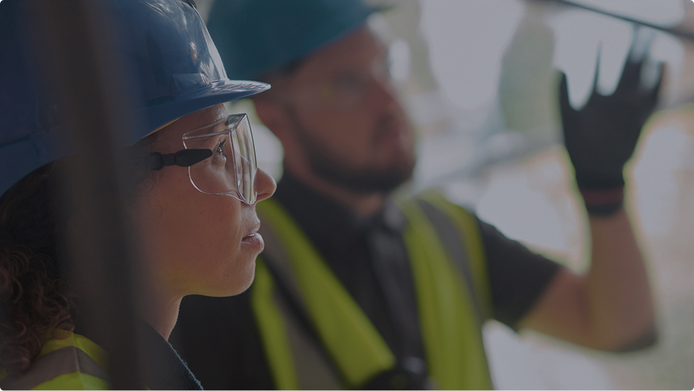 Close-up of a person wearing safety glasses and a blue hard hat with the text 'EMISSIONS Low emissi project timel'.