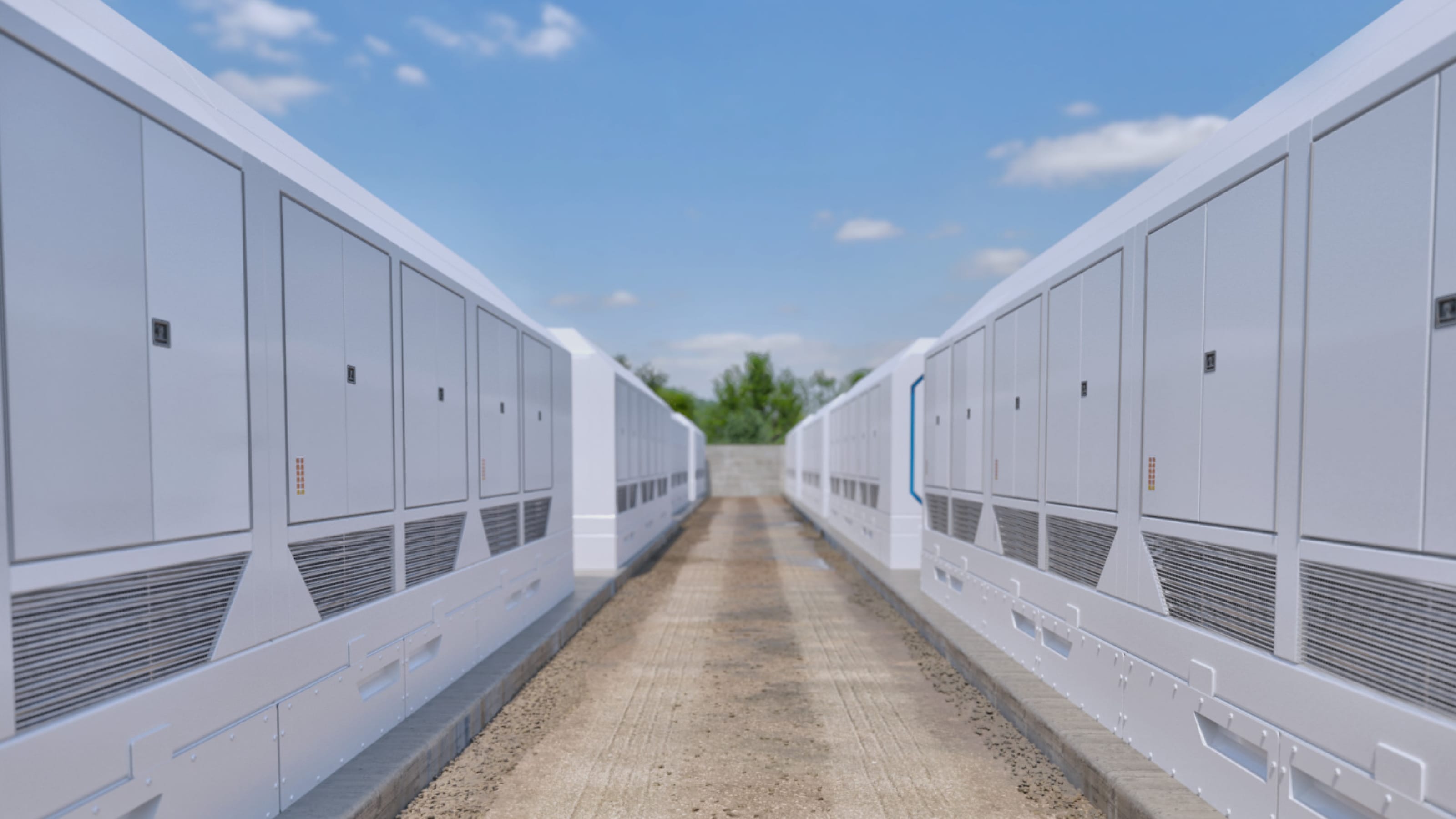 Two rows of large white industrial electrical cabinets facing each other along a gravel path under a partly cloudy sky.