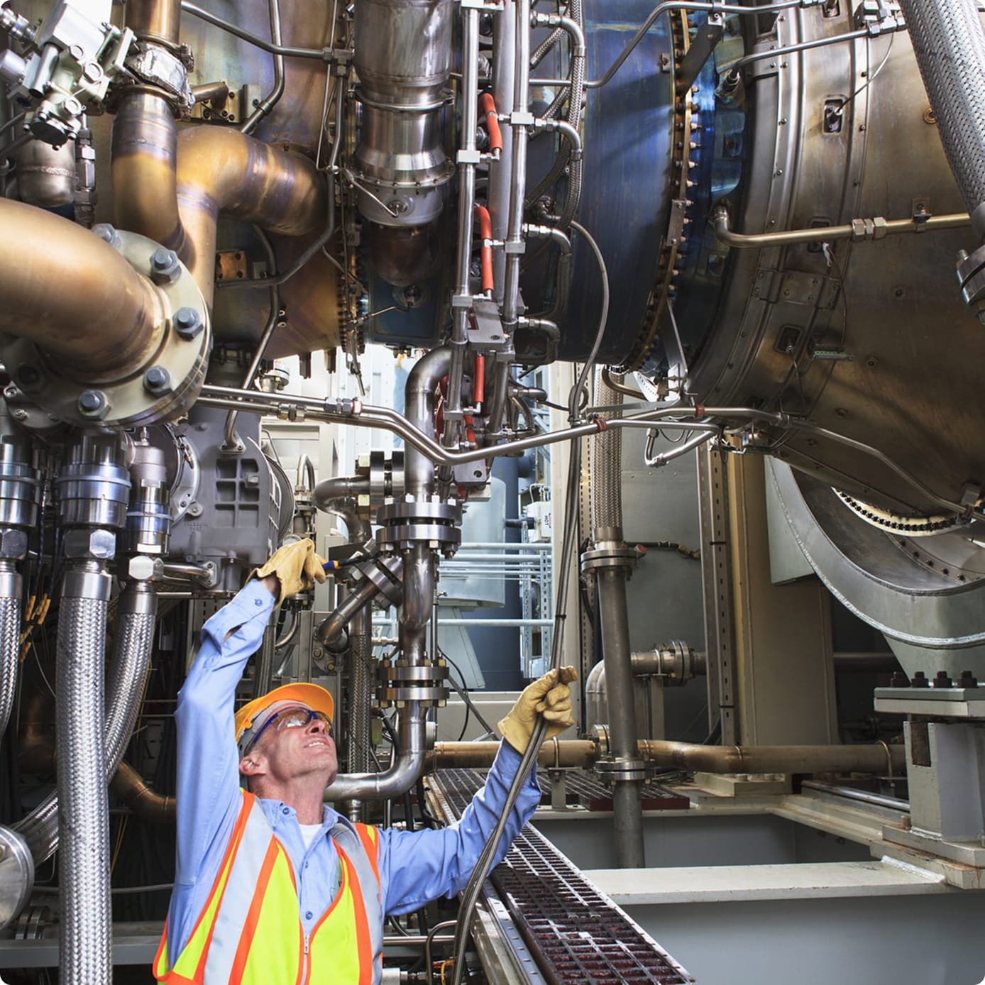 Engineer in safety gear inspecting and adjusting industrial pipes and machinery in a turbine room.