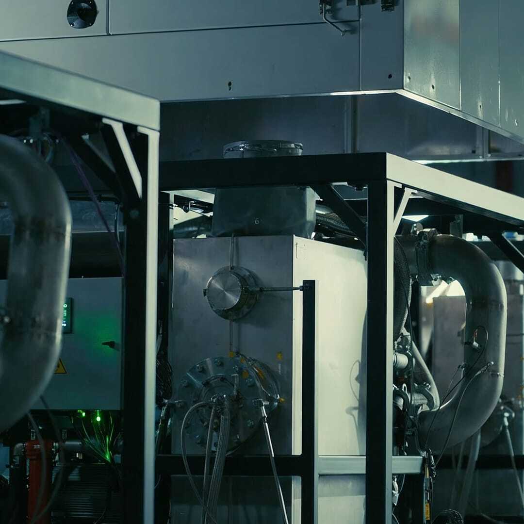 Industrial machinery with metal pipes and a large vent or duct system in a factory setting.