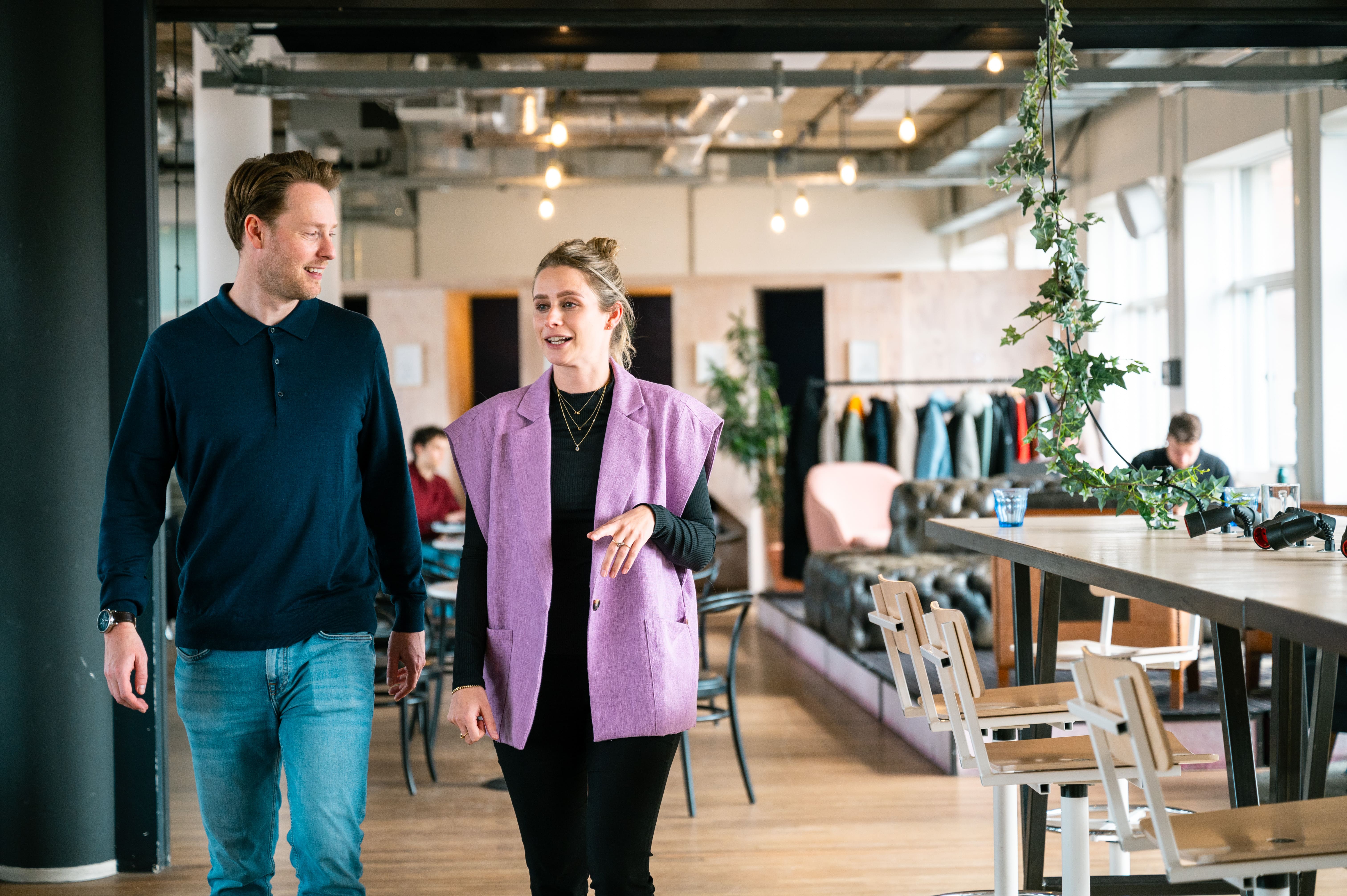 Vier groeileaders zitten en staan rond een tafel terwijl ze samen naar een laptop kijken tijdens een meeting, met koffiekopjes op tafel.