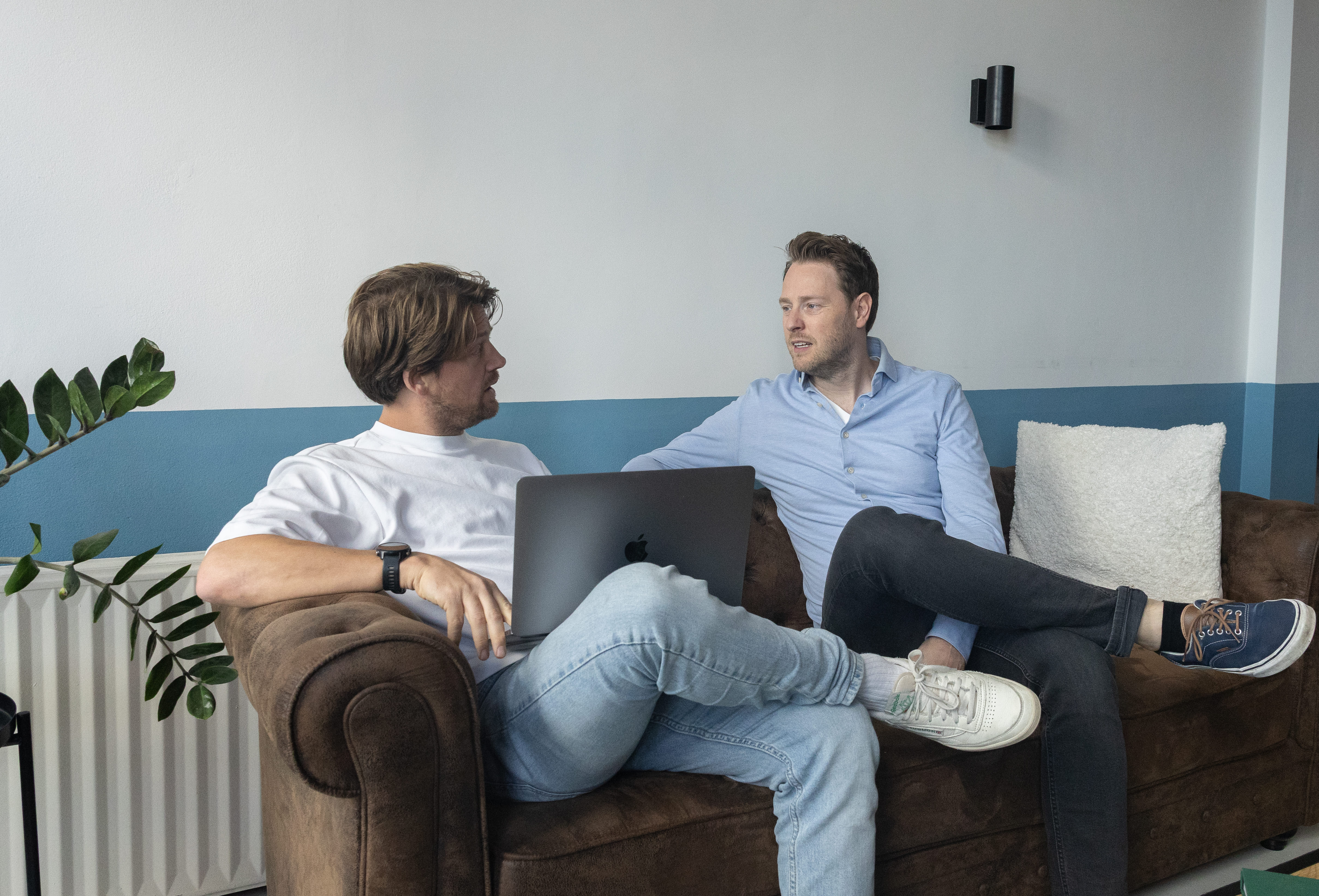 Drie groeileaders kijken samen lachend naar een laptop tijdens een overleg.