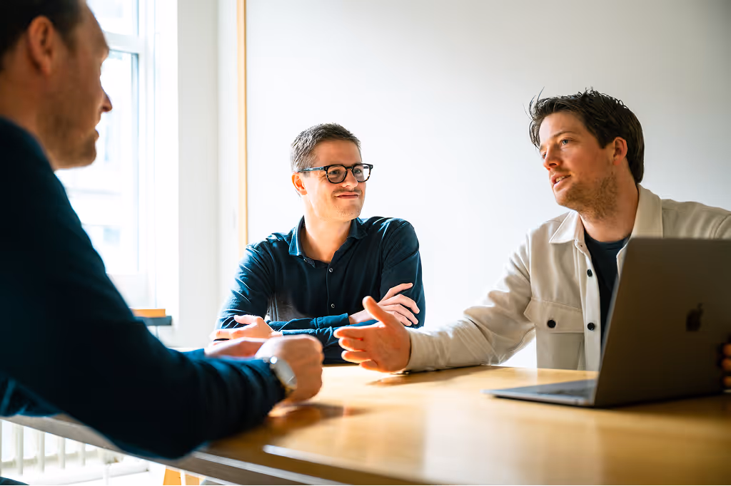 Team overlegt rond bureau met grafieken, sticky notes en tablet met dashboard in ochtendlicht