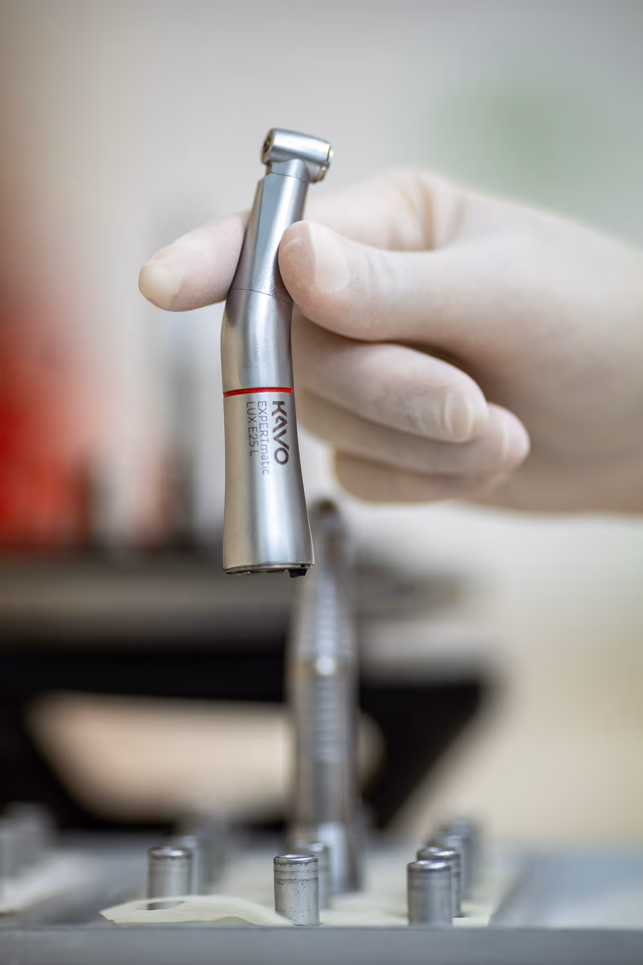 Hand in medizinischem Handschuh hält ein zahnärztliches Handstück mit der Aufschrift KAVO EXPERTmatic LUX E25 L.