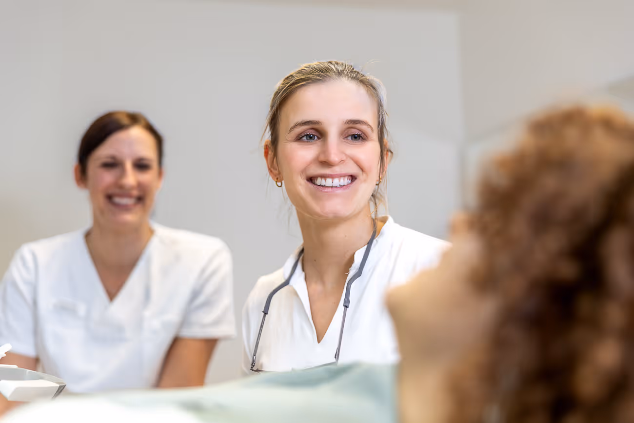 Lächelnde Zahnärztin und Assistenz an der Patientin