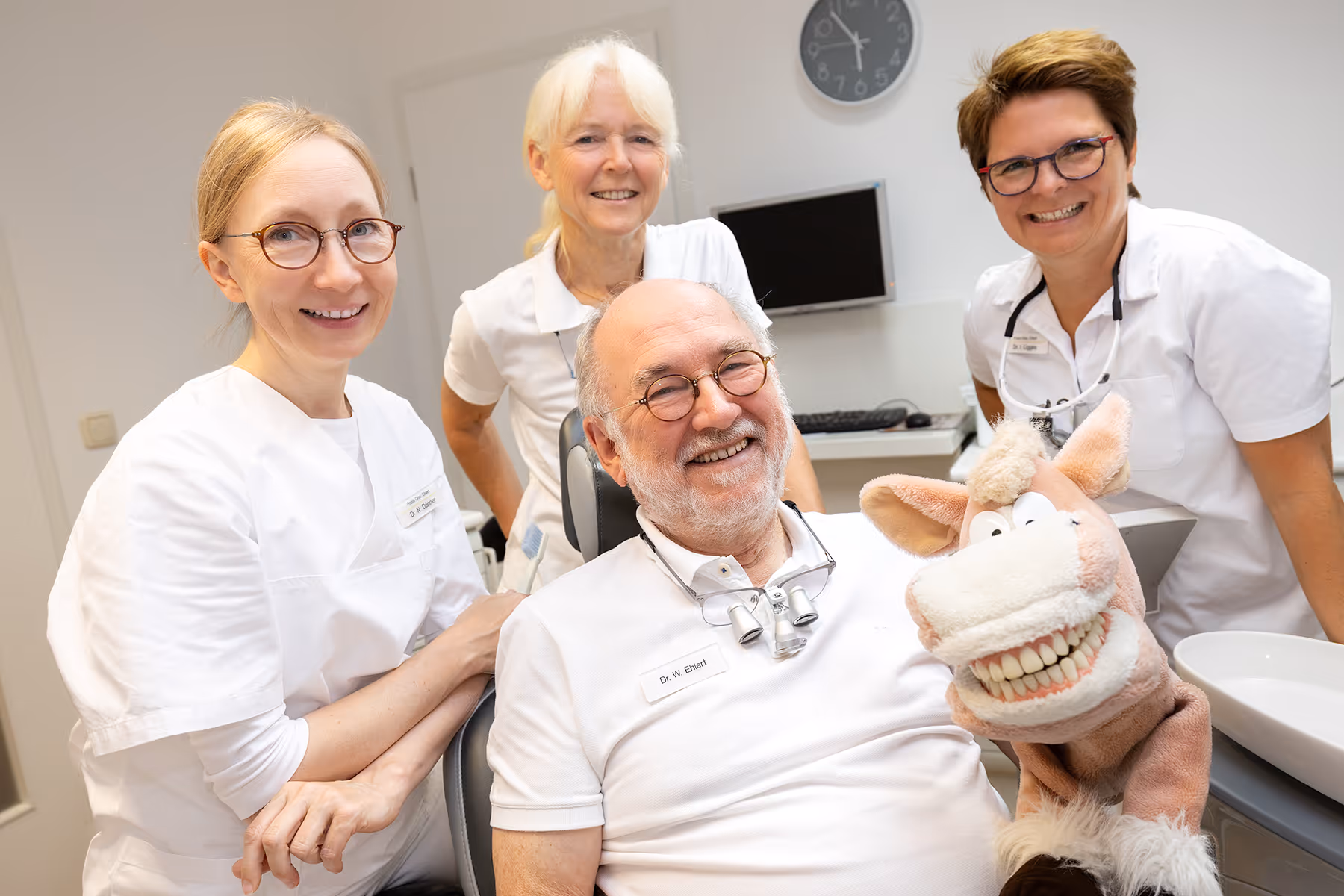 Die 4 Zahnärzte sitzen auf einem Behandlungsstuhl und Wolfgang hält Oskar die Zahnputz Handpuppe in der Hand. Alle freuen sich.