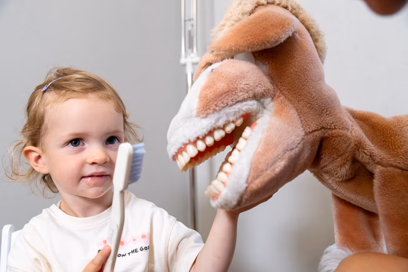Kleines Mädchen hält eine Zahnbürste und putzt die Zähne eines Dinosaurier-Plüschtiers.
