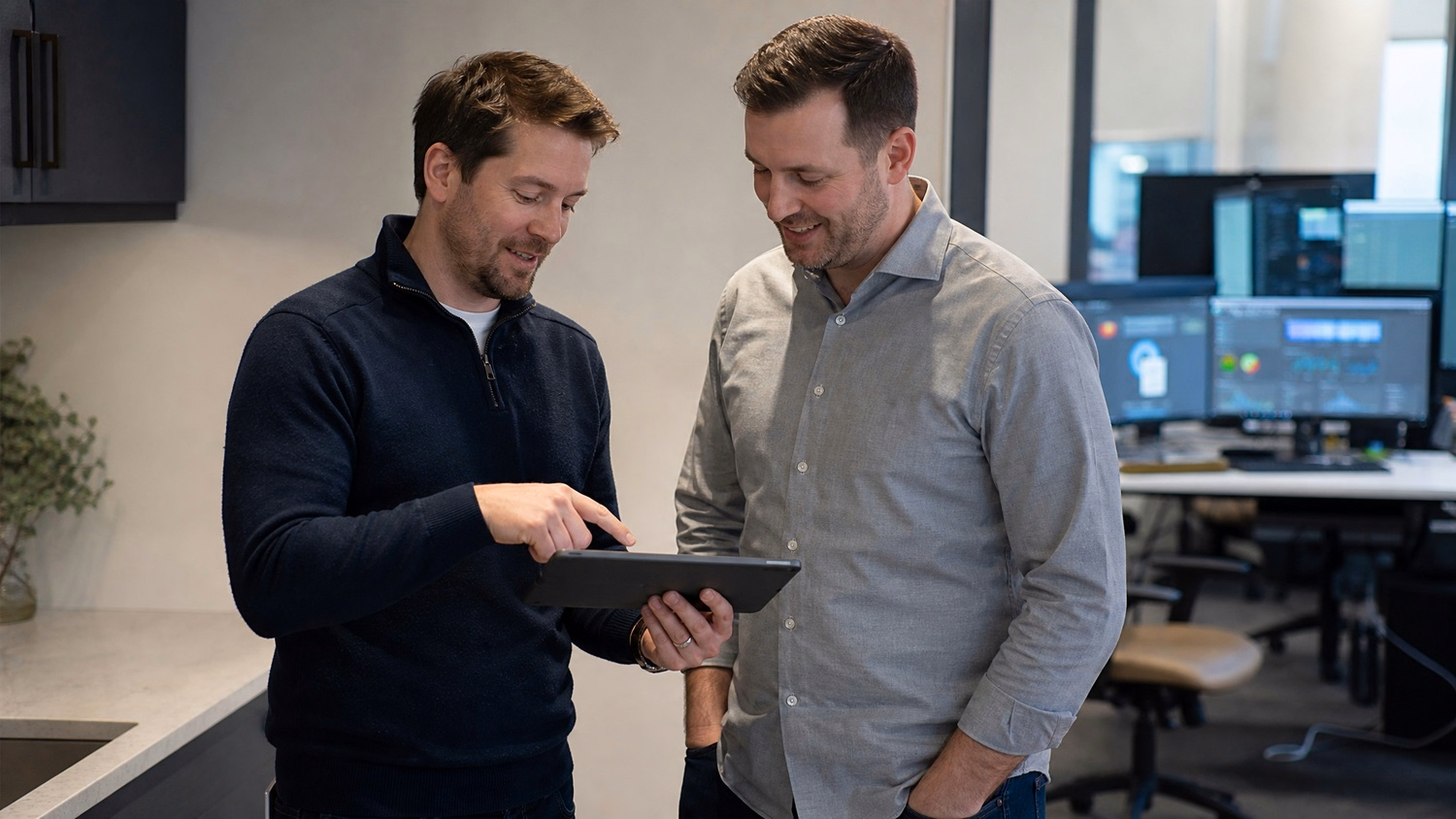 Two Caucasian men in their late 30s, dressed in casual business wear, are standi