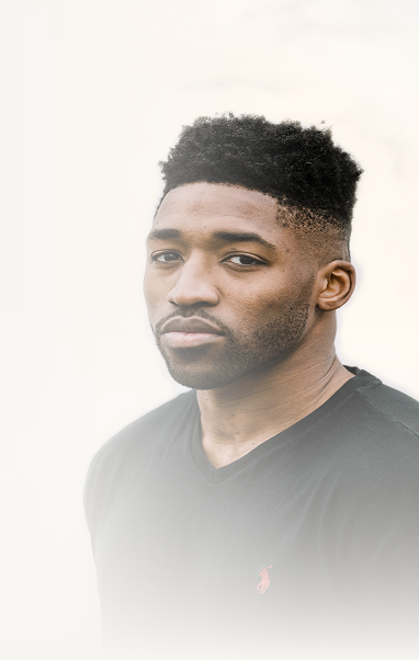 Portrait of Meech with short curly hair and a trimmed beard, wearing a black V-neck shirt.