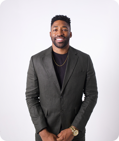 Meech Robinson (Meech) smiling in a dark blazer and black shirt standing against a plain white background.