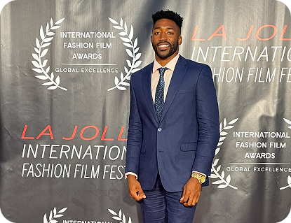 Meech Robinson (Meech) smiling in a navy blue suit posing at the La Jolla International Fashion Film Festival backdrop.