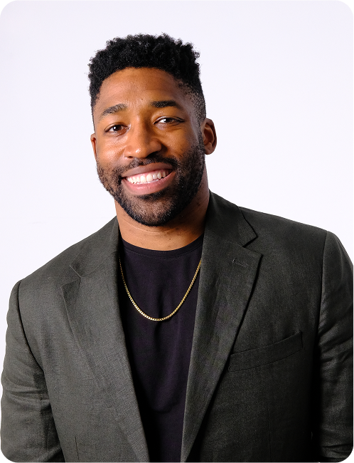 Meech smiling wearing a dark green blazer, black shirt, and gold chain necklace against a white background.