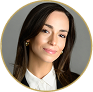 Professional headshot of a woman with long dark hair wearing a white shirt and dark blazer, smiling slightly.