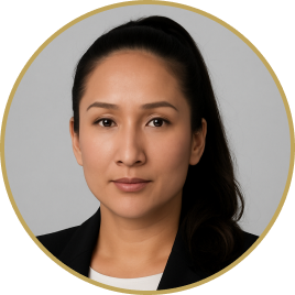 Portrait of a woman with long dark hair in a ponytail, wearing a black blazer and white shirt, against a gray background.