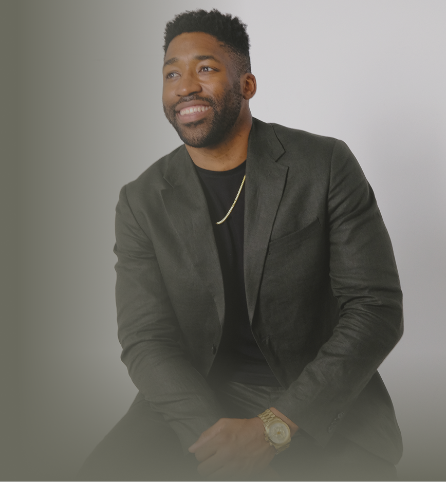 Meech smiling wearing a dark blazer, black shirt, gold chain, and gold watch against a plain light background.