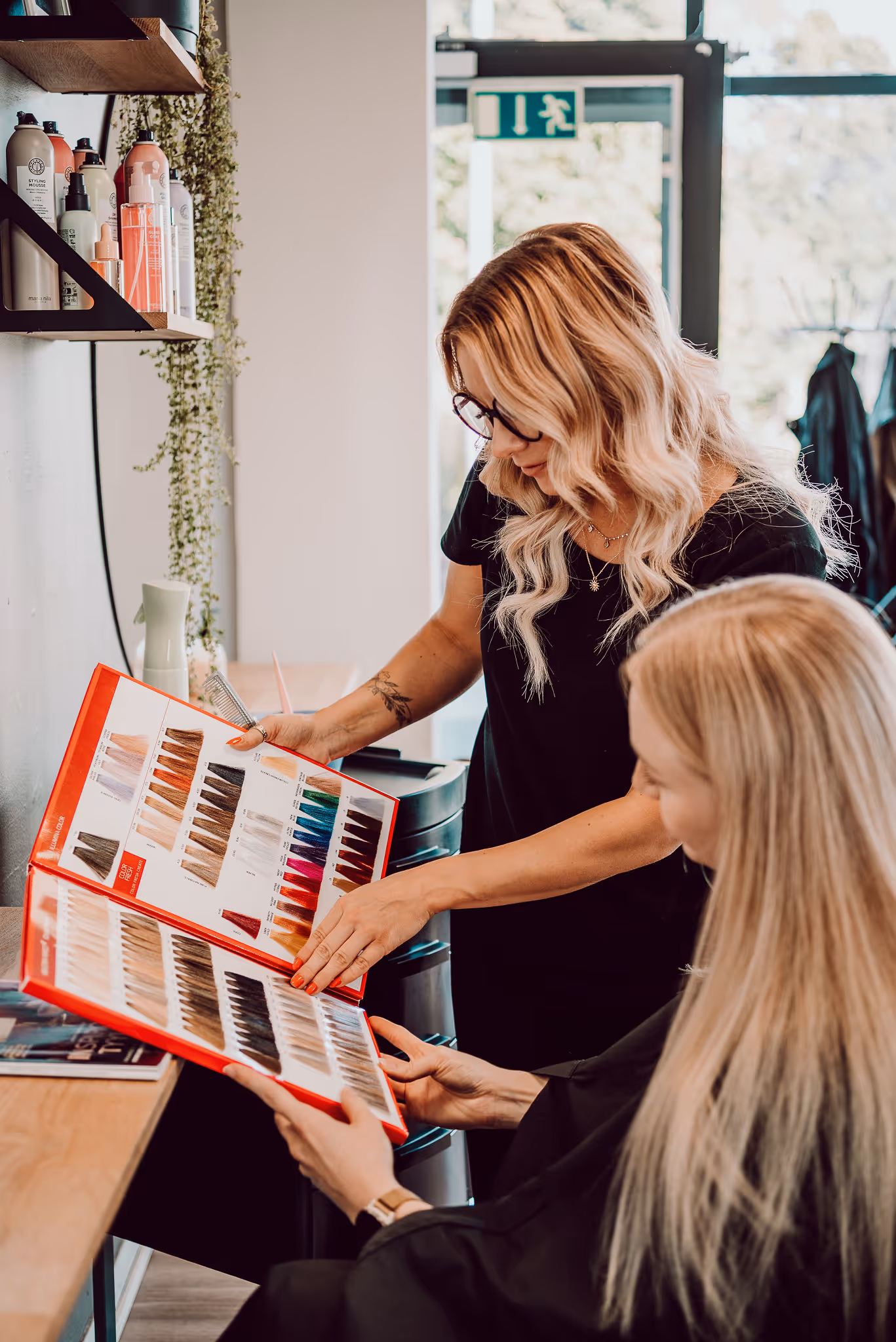 Kampaaja valitsemassa asiakkaan kanssa hiuksille väriä hoitolassa Kauneuspiste Riikka Mikkola