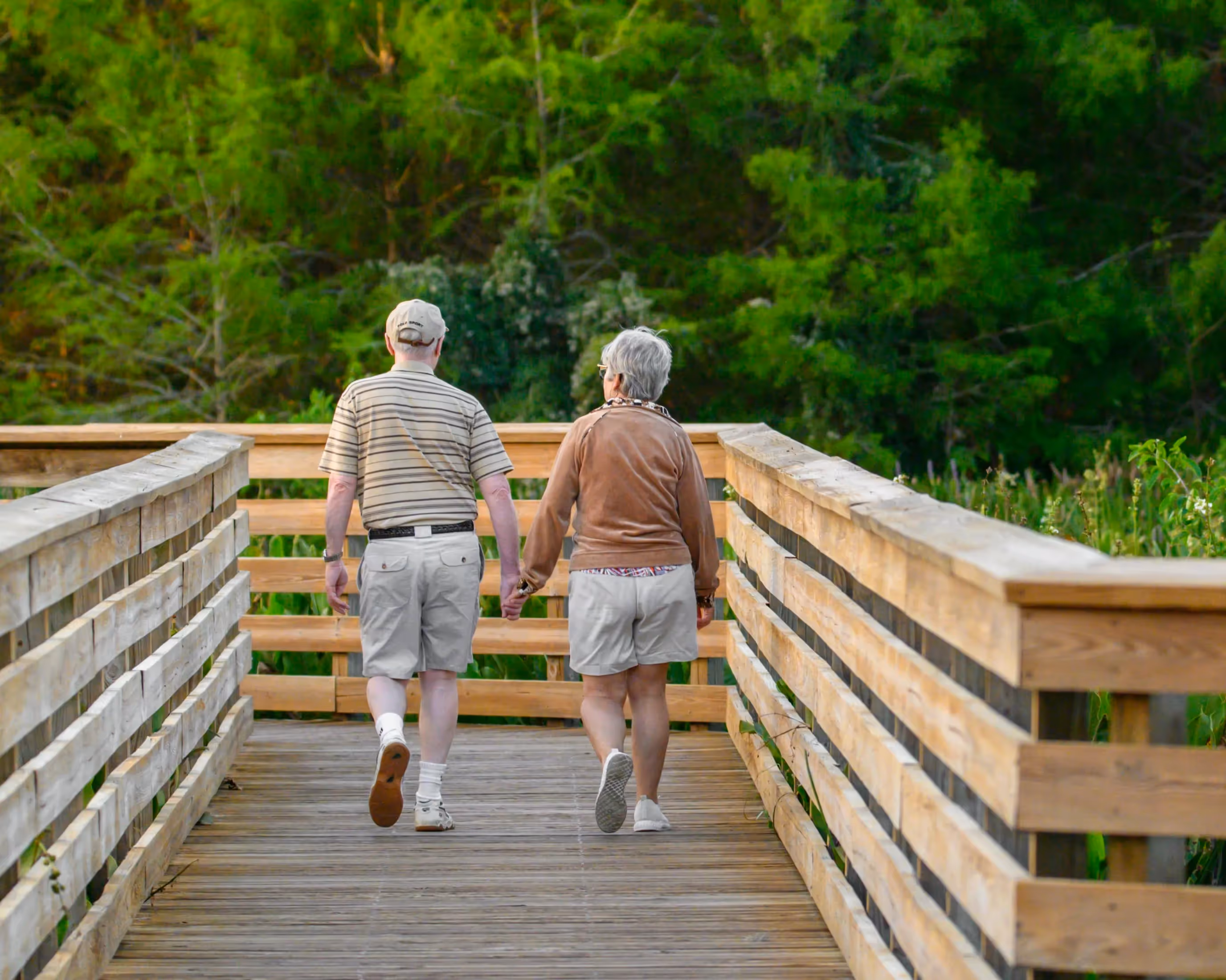 An elder couple holds hand while walking down a path.