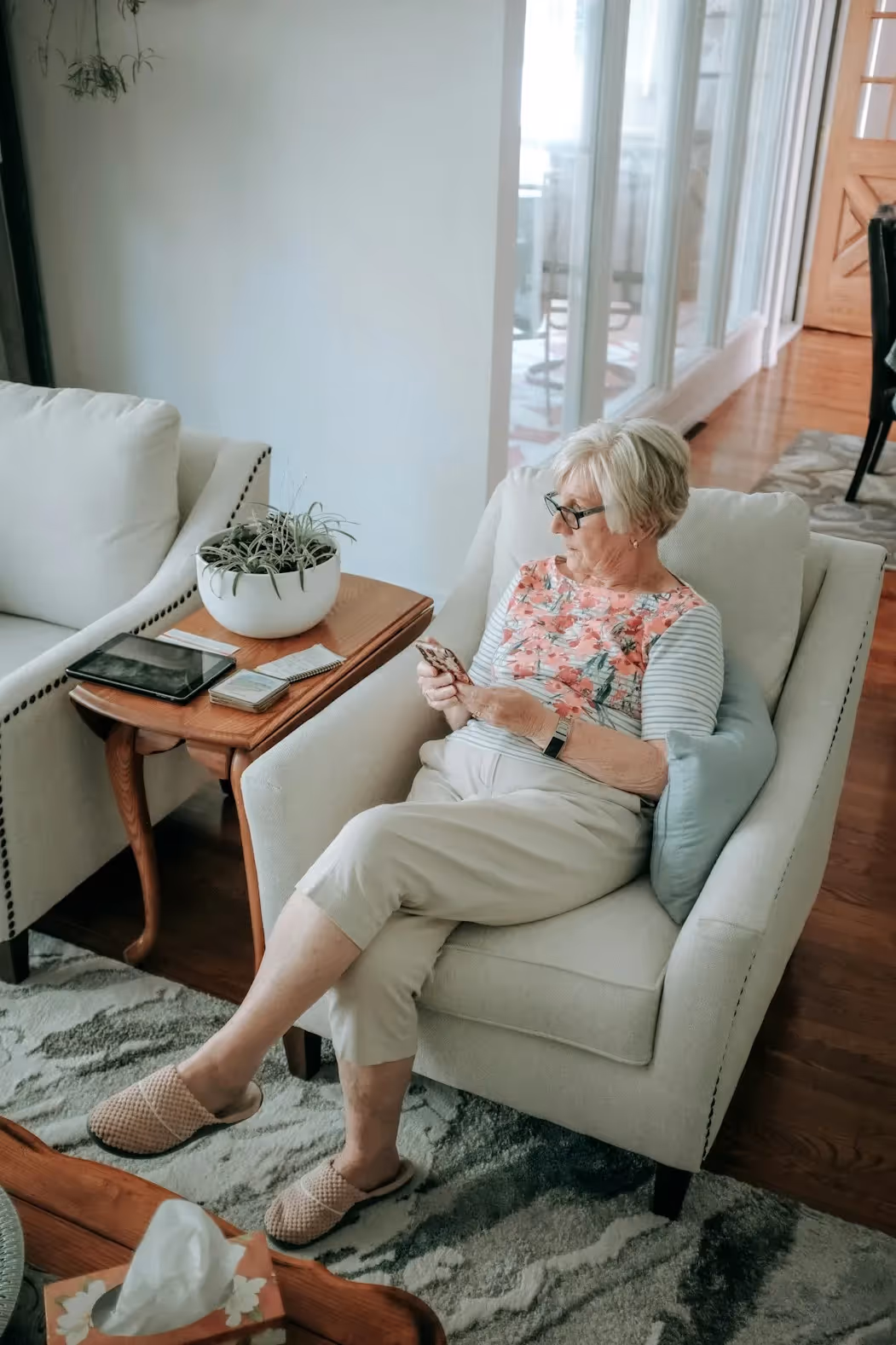An old lady sits on a couch, holding her phone while she chats with somebody not included in the picture.