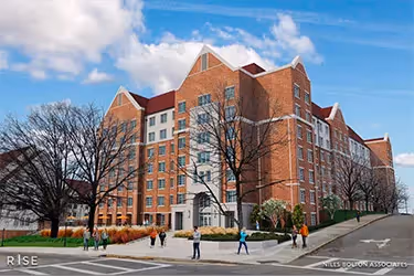 An artist rendering shows a large, seven-story building with orange brick, light tan accents and and a pitched red roof.