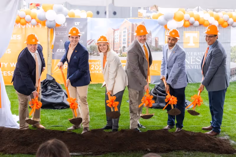 A group of people happily pose for a picture while holding shovels and dropping dirt on a path.