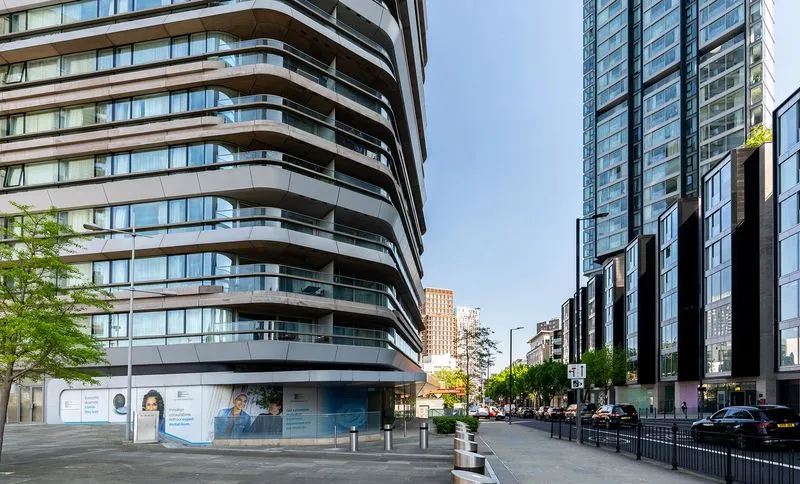 Modern curved apartment building on the left and tall glass buildings on the right along a city street under a clear blue sky.
