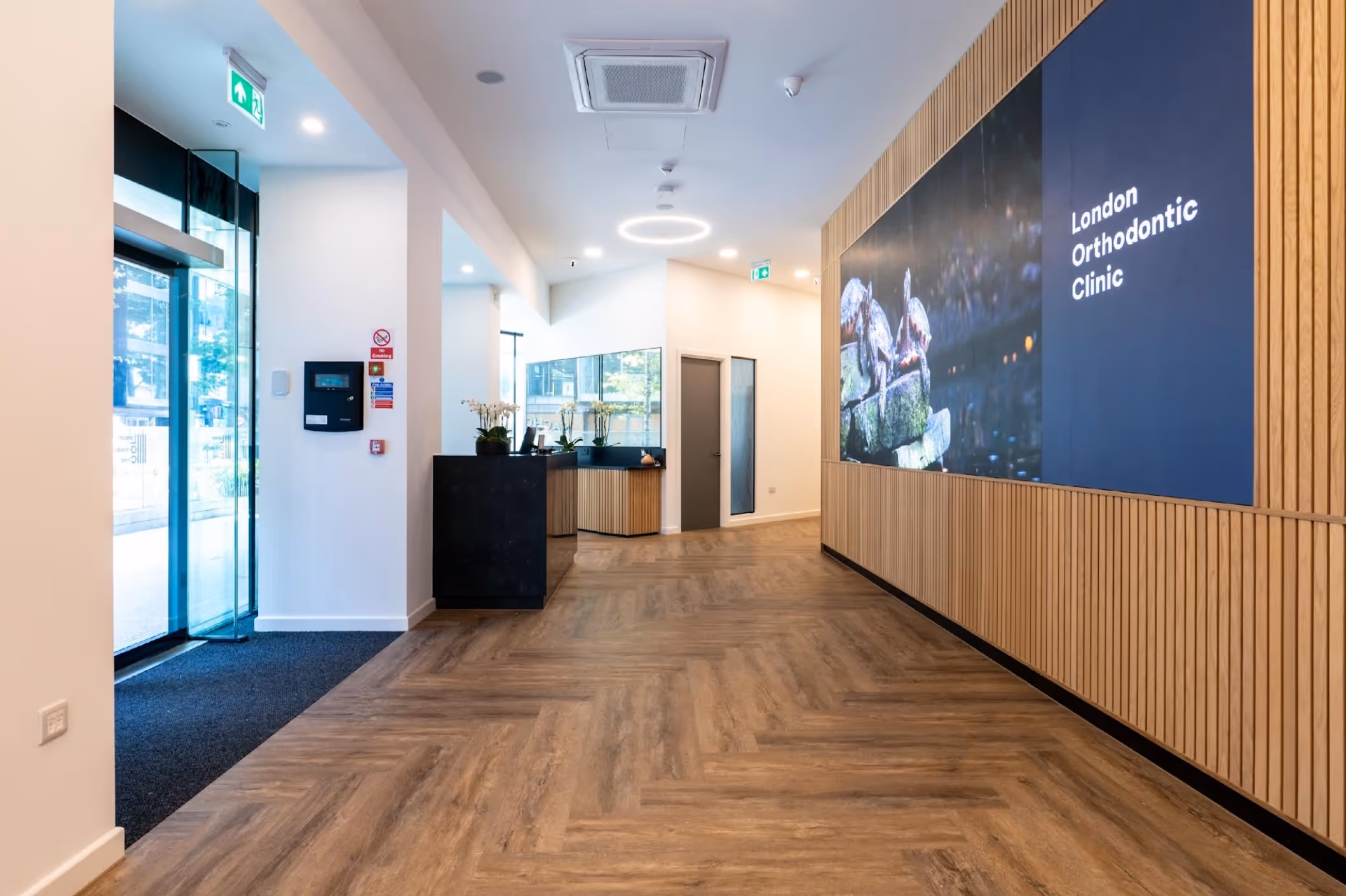 Reception area of London Orthodontic Clinic with wooden floor, modern desk, and large digital wall display.