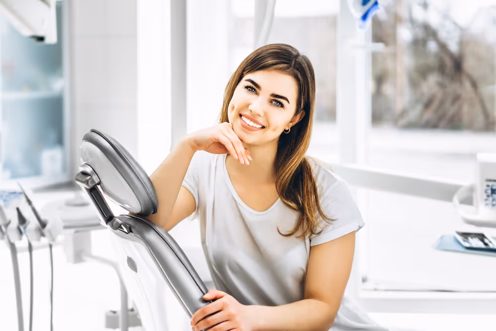 Smiling woman leaning on the backrest of a dental chair in a bright dental clinic.