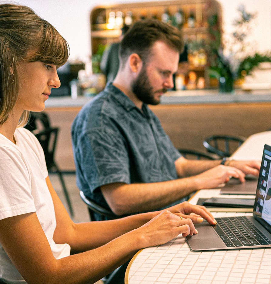 Two people sitting at a table working on laptops in a casual indoor setting.
