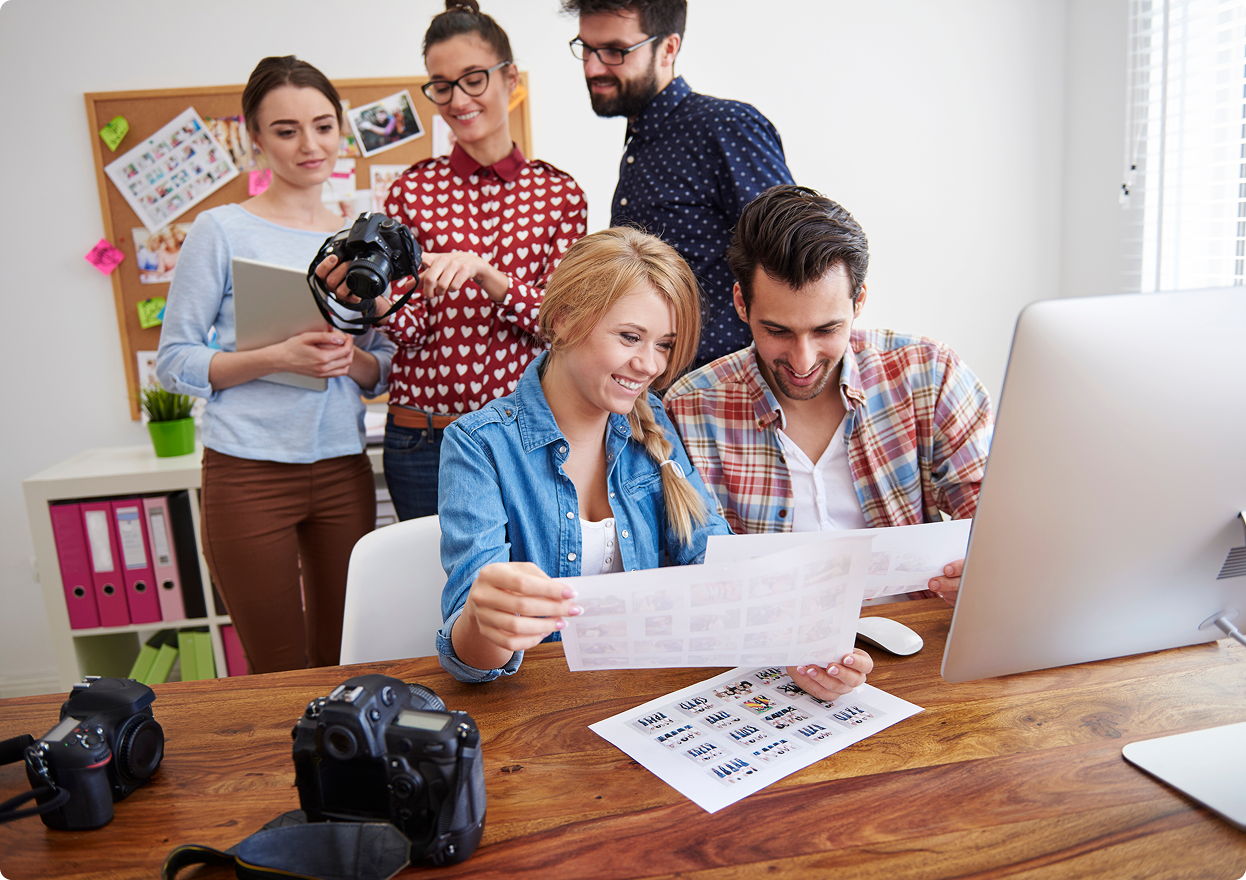 Group of young creative professionals reviewing photo prints and camera equipment in a bright office.