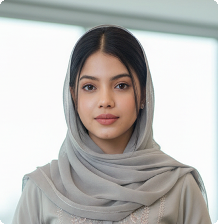Young woman wearing a light gray hijab and beige outfit looking directly at the camera.