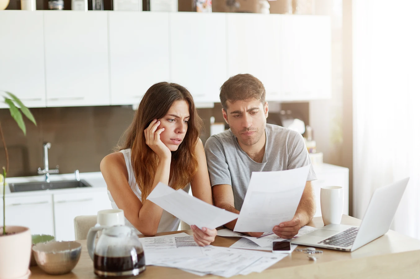 Couple sitting at a kitchen table looking worried while reviewing documents and bills.