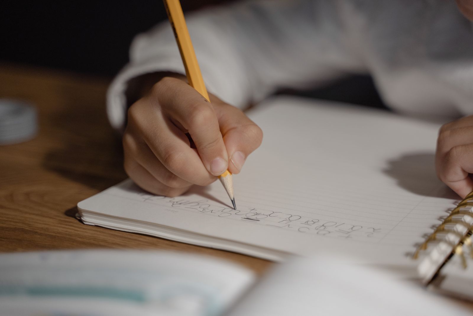 A child's hand writing in an exercise book with a pencil