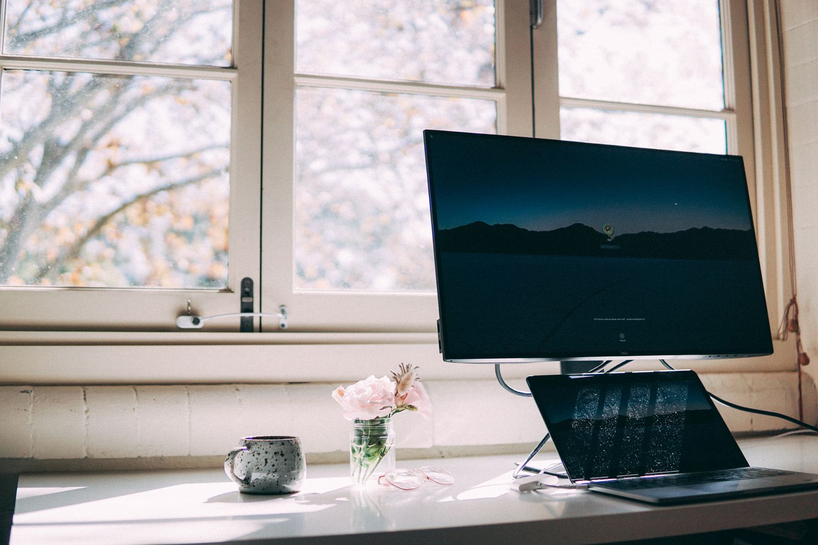 Home office desk by a window with a computer and flowers