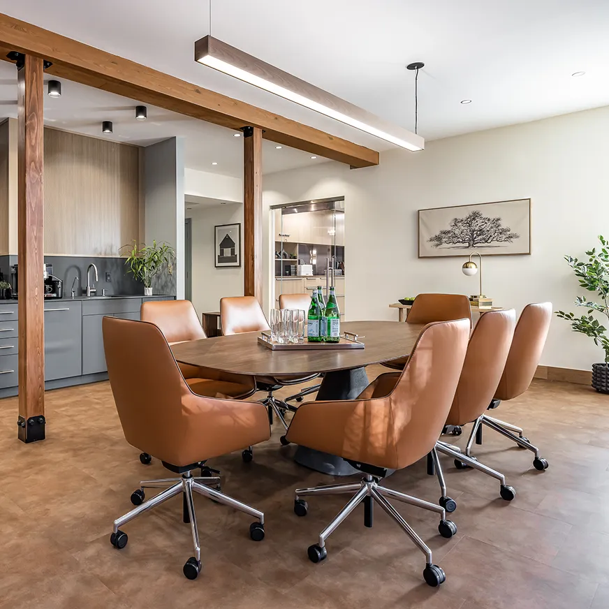 Stylish meeting room with brown leather chairs around a wood table and built-in kitchenette background.