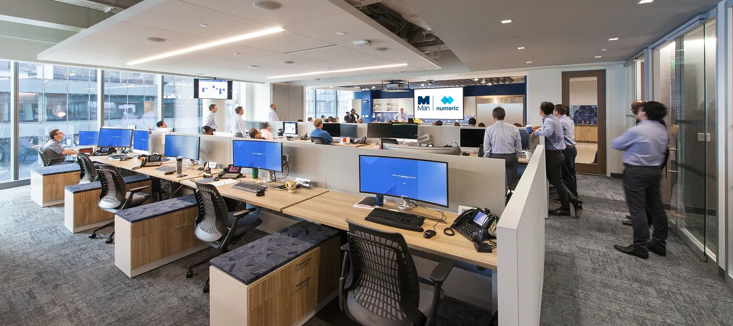 Modern open office with multiple workstations, desktop monitors, and employees collaborating in a bright professional workspace.