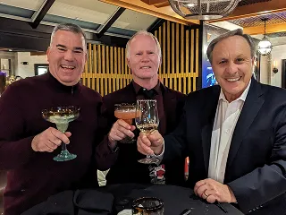 Three men smiling and raising glasses at a team dinner celebration.