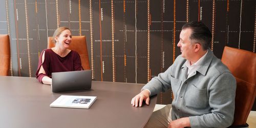 A man and a woman sitting around a conference room table smiling.