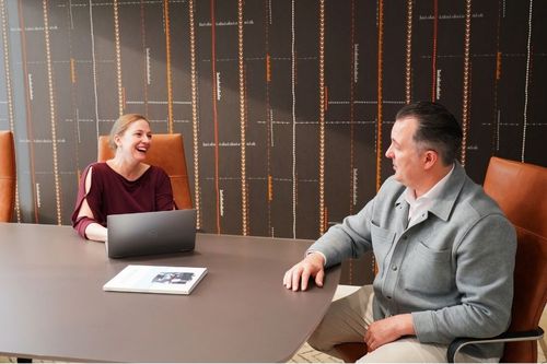 A man and a woman sitting around a conference room table smiling.