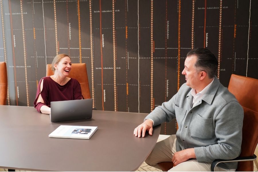 A man and a woman sitting around a conference room table smiling.