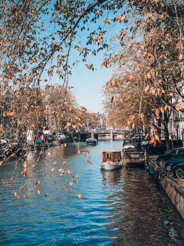 A scenic canal in autumn with boats on the water and leafless trees overhanging under a clear blue sky.