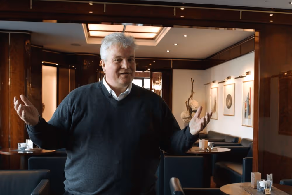 Älterer Mann gestikuliert in einem eleganten Café mit offenen Händen