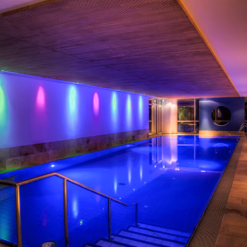 Beleuchteter Innenpool mit lila und blauem Ambiente und Treppe