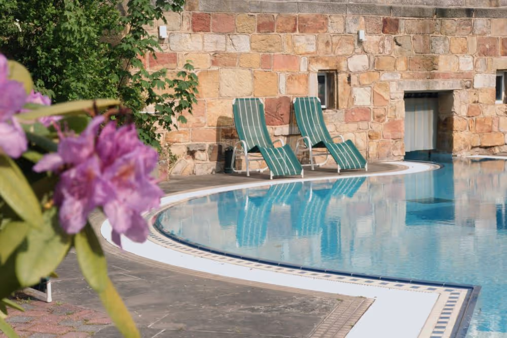 Blauer Swimmingpool mit gestreiften Liegestühlen an Natursteinmauer