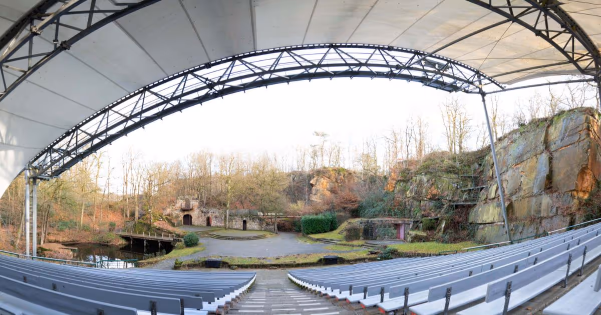 Überdachtes Freilichttheater mit Steinwänden und Sitzreihen im Wald