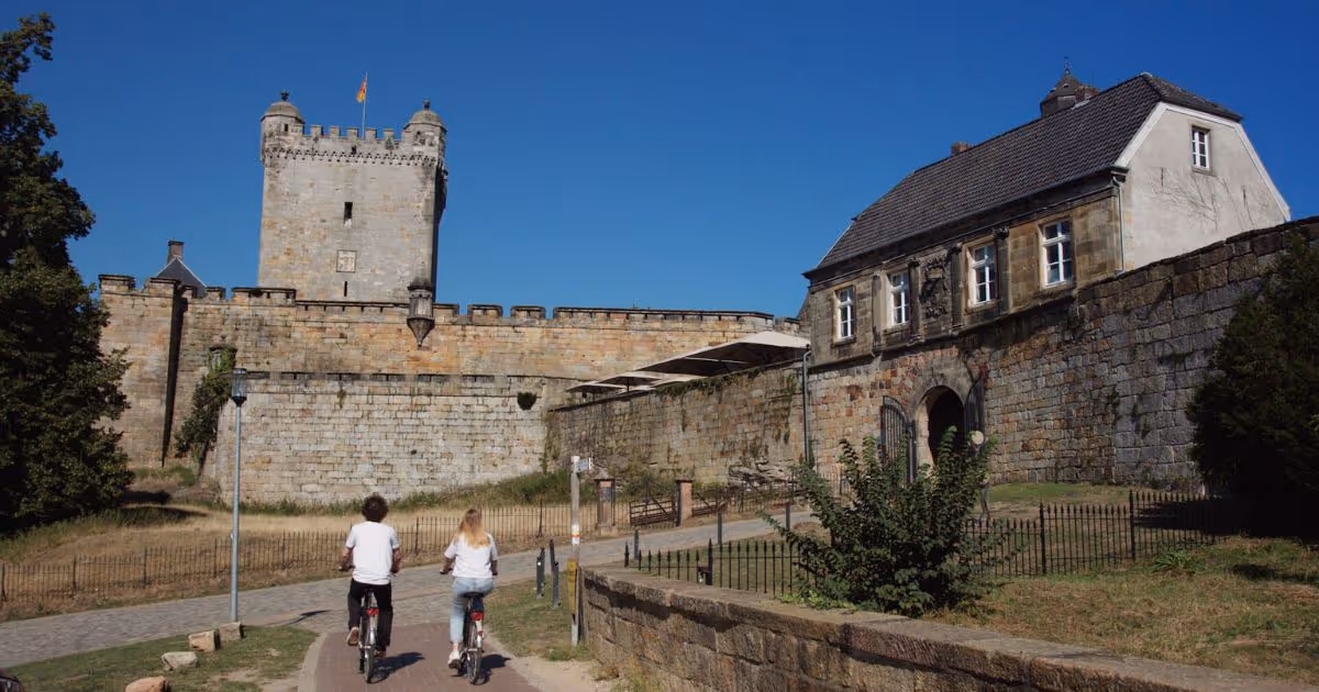 Zwei Radfahrer neben historischer Burgmauer an sonnigem Tag