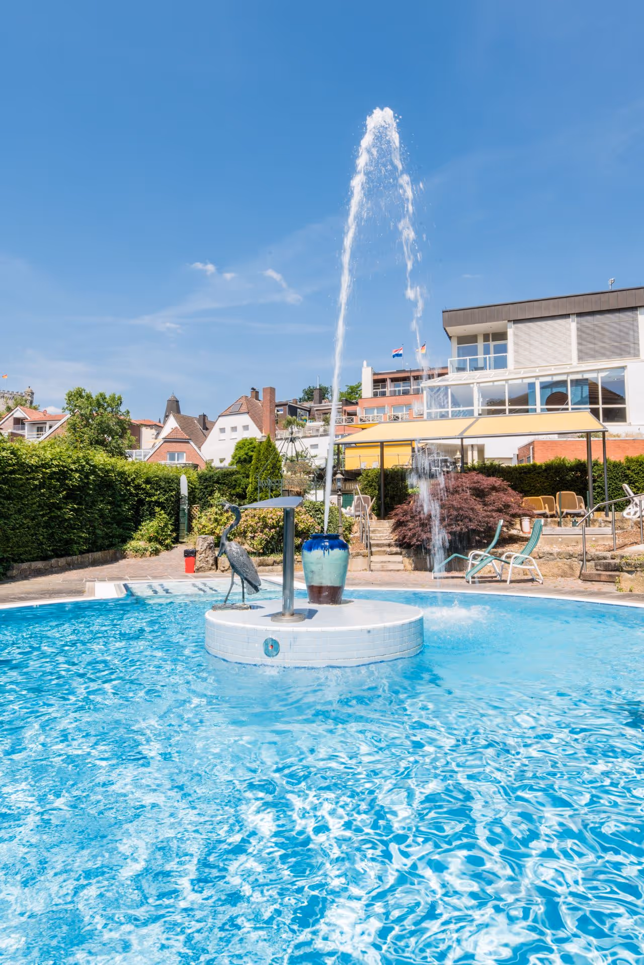 Blauer Swimmingpool mit Springbrunnen und Reiher-Skulptur an sonnigem Tag