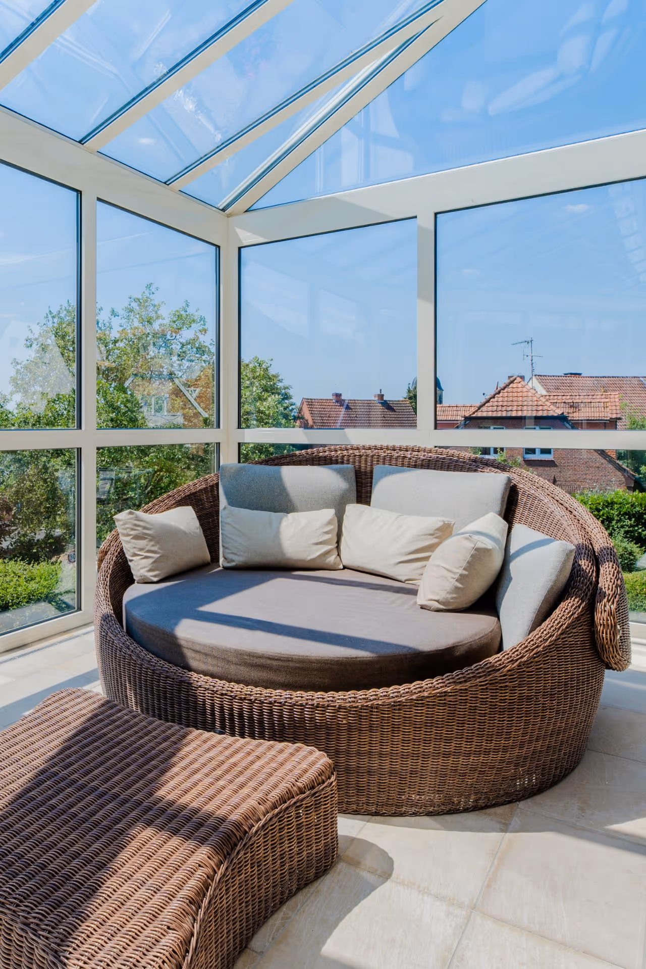 Rundes Rattansofa in hellem Wintergarten mit Glaswänden und Ausblick